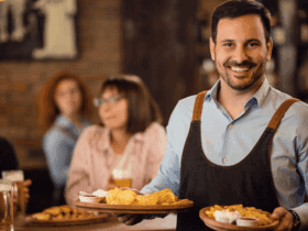 Smiling restaurant server delivering food to happy guests in a casual dining setting, representing improved customer experience with Applova’s email marketing tools.