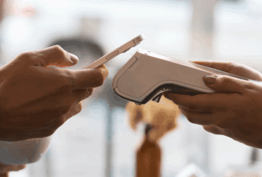 Customer making a contactless payment using a smartphone at a restaurant counter with a handheld POS device.
